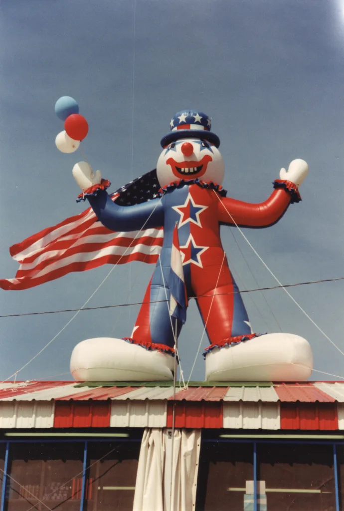 heritage-molly-browns-valley-park-clown Historic Molly Brown’s Fireworks photo of a giant patriotic inflatable clown holding balloons and an American flag on the store roof.