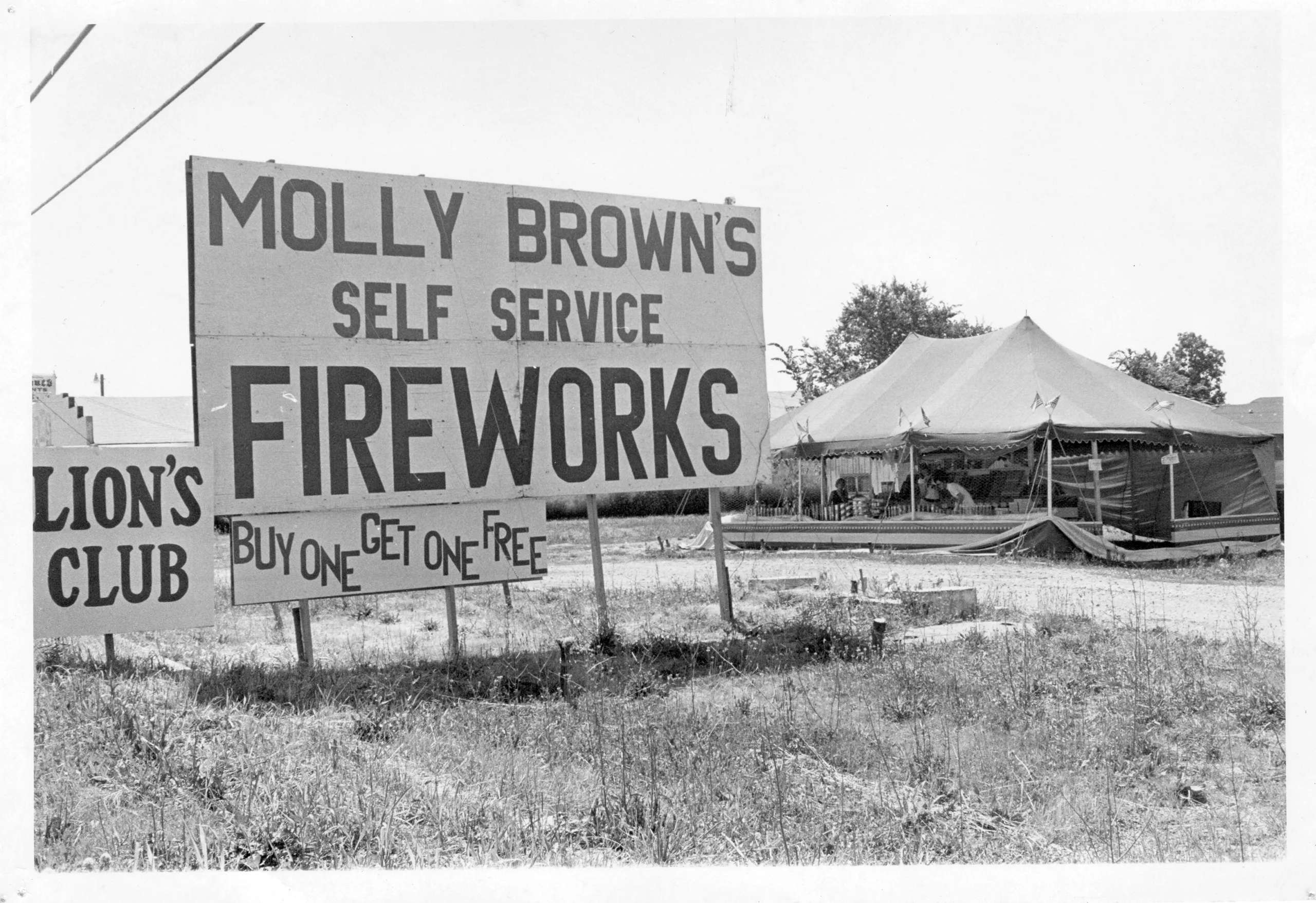 Historic black-and-white photo of an early Molly Brown’s Fireworks tent with a large self-service fireworks sign and buy-one-get-one-free promotion.