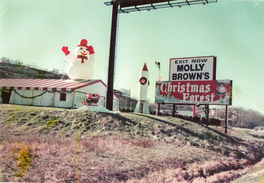 heritage-molly-browns-christmas-forest-2 Historic photo of Molly Brown’s Christmas Forest with a roadside sign, striped tent, inflatable snowman, and rocket decoration.