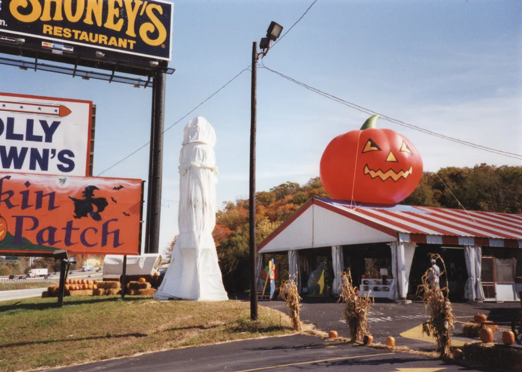 heritage-molly-browns-pumpkin-patch-2 Historic Molly Brown’s Pumpkin Patch display with a large inflatable jack-o’-lantern, roadside signage, hay bales, corn stalks, and a striped tent.