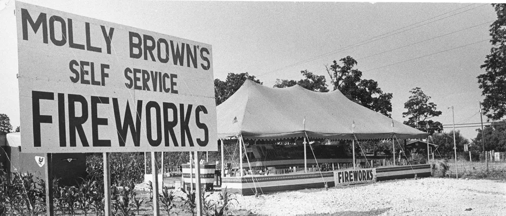 heritage-molly-browns-self-service-fireworks Historic black-and-white photo of a Molly Brown’s Fireworks roadside tent beside a large sign reading “Molly Brown’s Self Service Fireworks.”