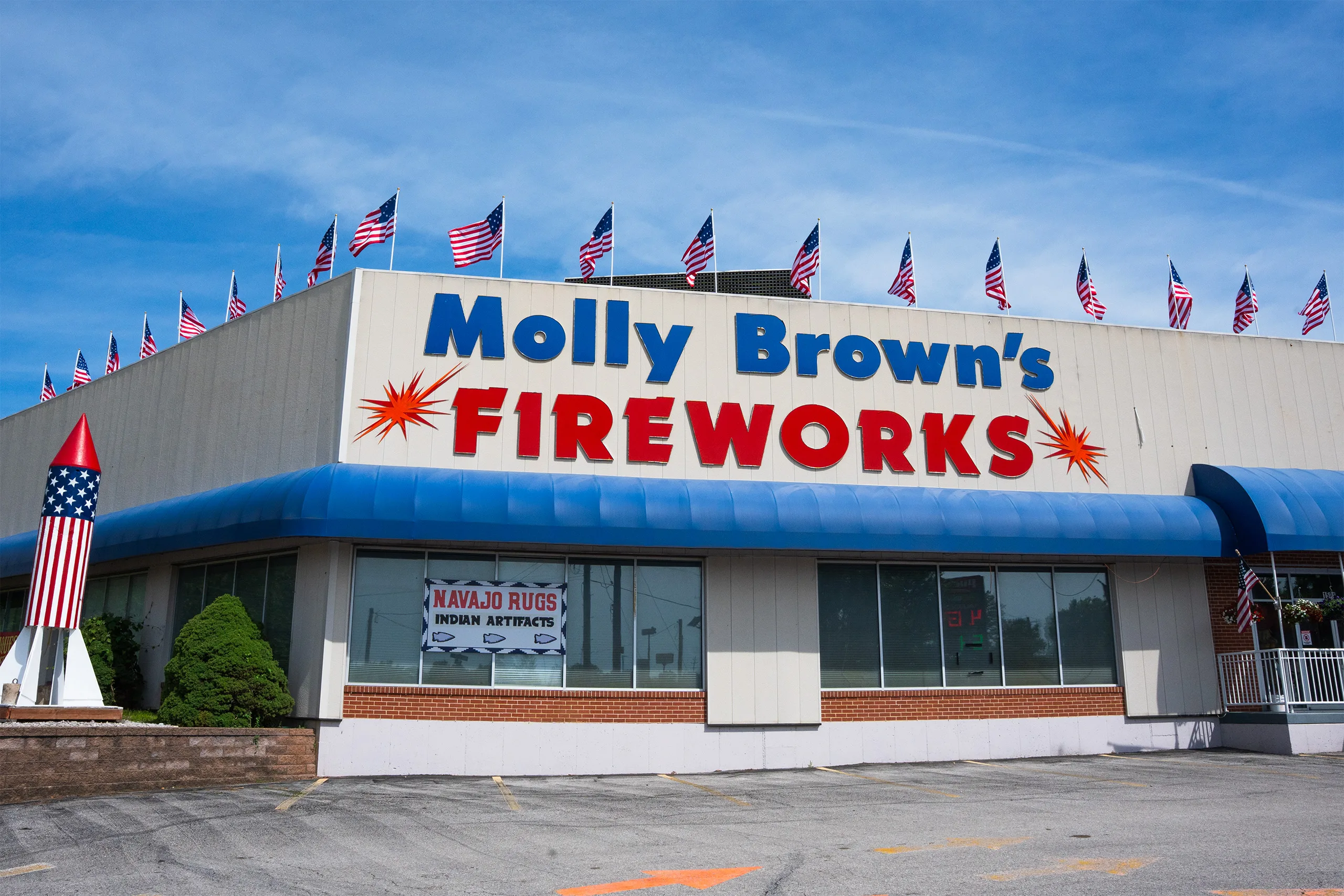 Exterior of the Molly Brown’s Fireworks store with large red and blue signage, a blue awning, and American flags flying along the roof.